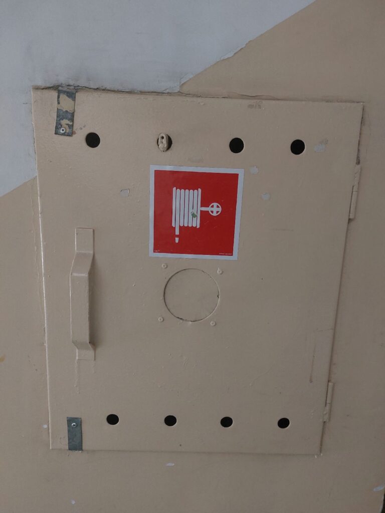 Zanitowana szafka z wężem gaśniczym, uniemożliwiająca szybki dostęp w razie pożaru